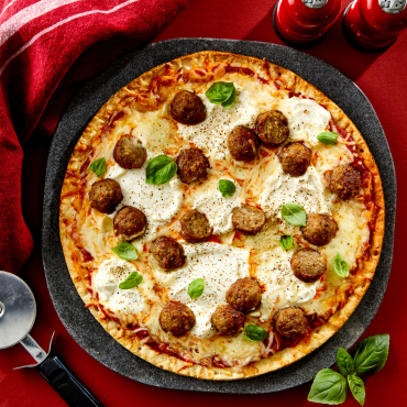 Meatball pizza with ricotta and basil leaves on a cloth background with pizza cutter